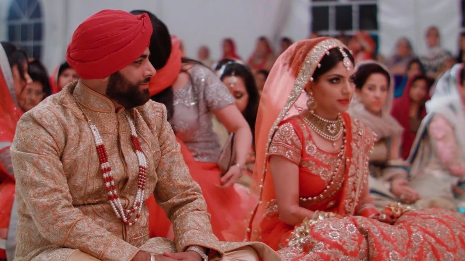 Multi-day wedding film still of Aseem and Hargunn seated with family and guests at their wedding ceremony