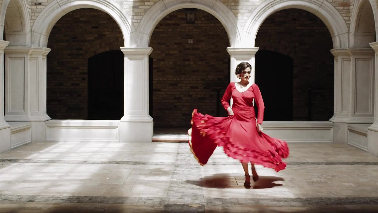 Spain destination wedding inspiration: a dancer in a red dress turning in an arched stone courtyard, from our concept film The Secret of Flamenco